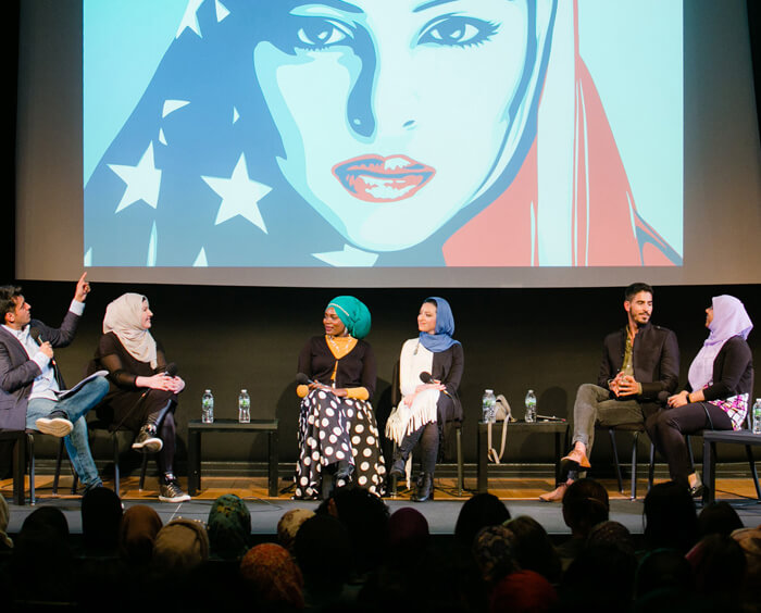 People on stage at a panel discussion pointing to an illustration of a woman wearing a hijab printed with the American flag