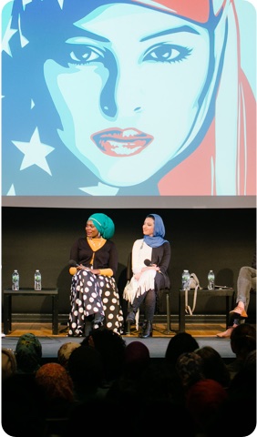 People on stage at a panel discussion pointing to an illustration of a woman wearing a hijab printed with the American flag